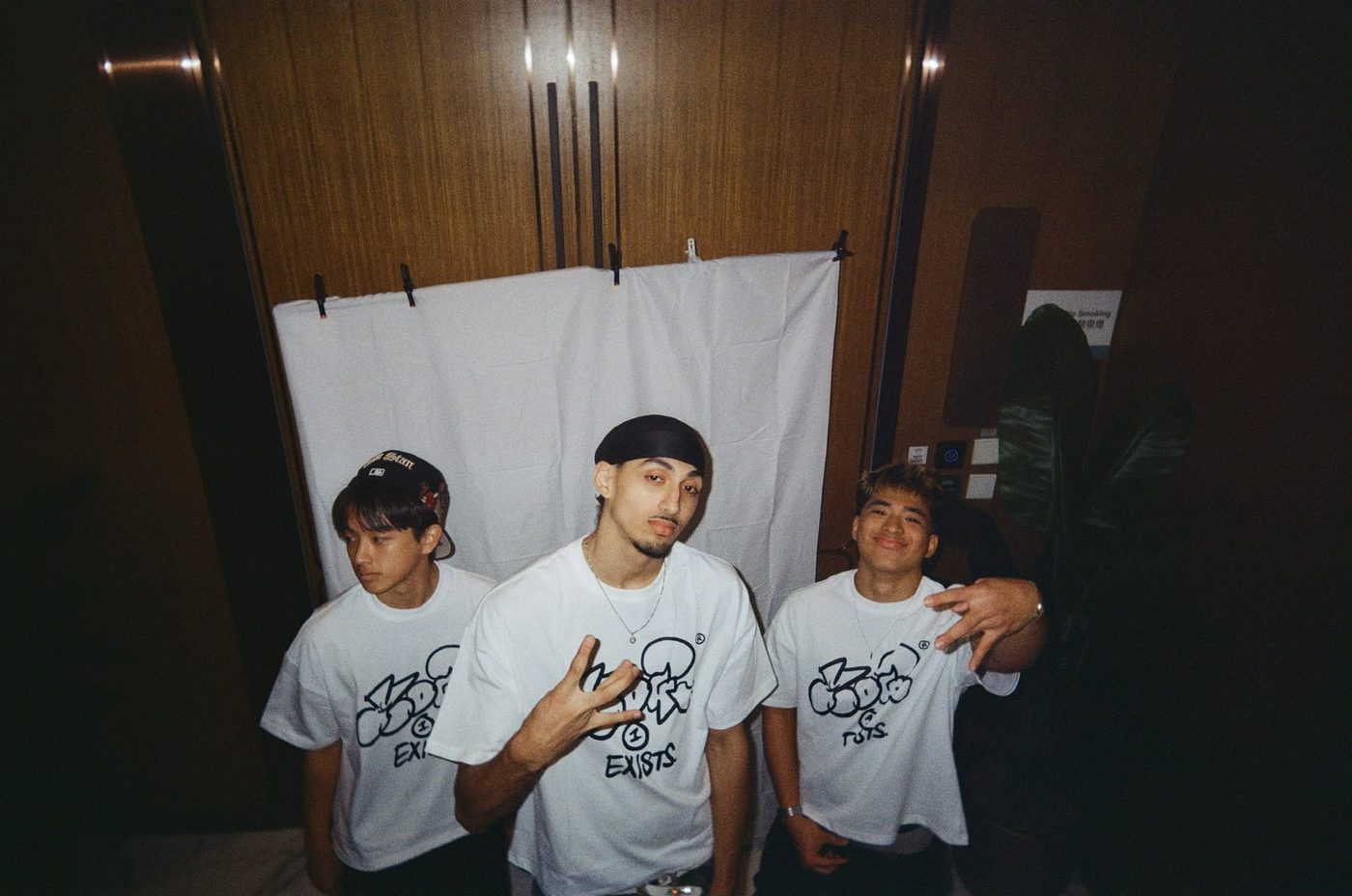 Three people in Drop 0 tees against a hung white sheet
